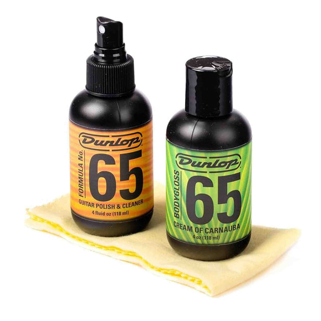 The image shows two Dunlop Formula 65 guitar care products: a 4 oz black spray bottle of Guitar Polish & Cleaner with an orange label, and a 4 oz black flip-top bottle of Cream of Carnauba with a green label. A yellow textured polishing cloth is also included. These products are used to clean, polish, and protect guitar finishes, helping maintain the instrument’s appearance and condition.
