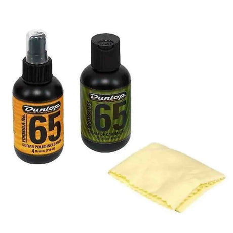 The image shows a Dunlop guitar care kit featuring two bottles of Formula 65 guitar maintenance products—one orange-labeled guitar polish & cleaner spray and one green-labeled cleaner or conditioner—alongside a light yellow microfiber cloth. This kit is designed to clean, polish, and protect guitars, helping musicians maintain their instrument’s finish and playability.