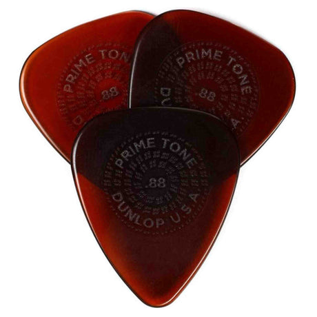 The image shows three Dunlop Primetone guitar picks with a teardrop shape and translucent amber finish. Each pick features embossed circular text reading "PRIME TONE" and "DUNLOP USA," along with a visible thickness of .88mm. Known for their premium construction and sculpted tips, these picks offer durability, good grip, and smooth string release, favored by guitarists for both acoustic and electric playing.