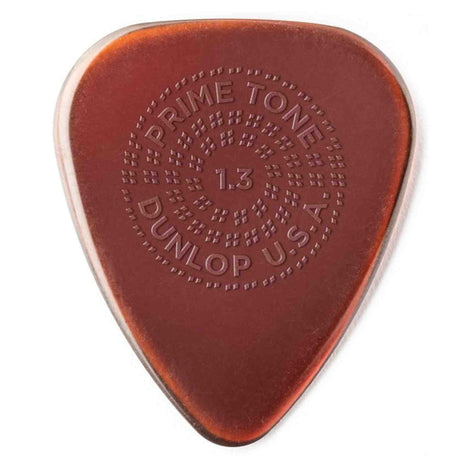 The image shows a Dunlop Primetone guitar pick, 1.3mm thick, in amber/tortoiseshell color. It features embossed circular text: "PRIME TONE" at the top, "1.3" in the center, "DUNLOP" at the bottom, and "U.S.A." on the side. Known for its smooth surface, durable build, and textured grip, this medium-heavy pick offers control and comfort, popular among guitarists across various genres.