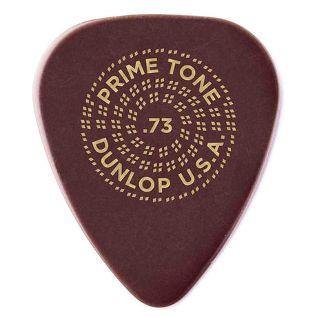 The image shows a Dunlop USA Primetone guitar pick, model .73mm thick, with a dark reddish-brown color. It features Dunlop’s circular logo with dotted patterns and the text "PRIME TONE," "DUNLOP USA," and ".73" in the center. This medium-gauge pick is made from premium materials, offering a balance of flexibility, control, tone, and durability for versatile guitar playing.