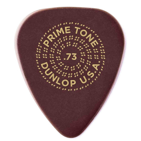 The image shows a Dunlop USA Primetone guitar pick with a .73mm thickness, printed in gold on its dark reddish-brown teardrop-shaped surface. Known for smooth play and durability, this medium-gauge pick features a decorative circular dot pattern around the text, adding visual appeal and extra grip for strumming or picking guitar strings.