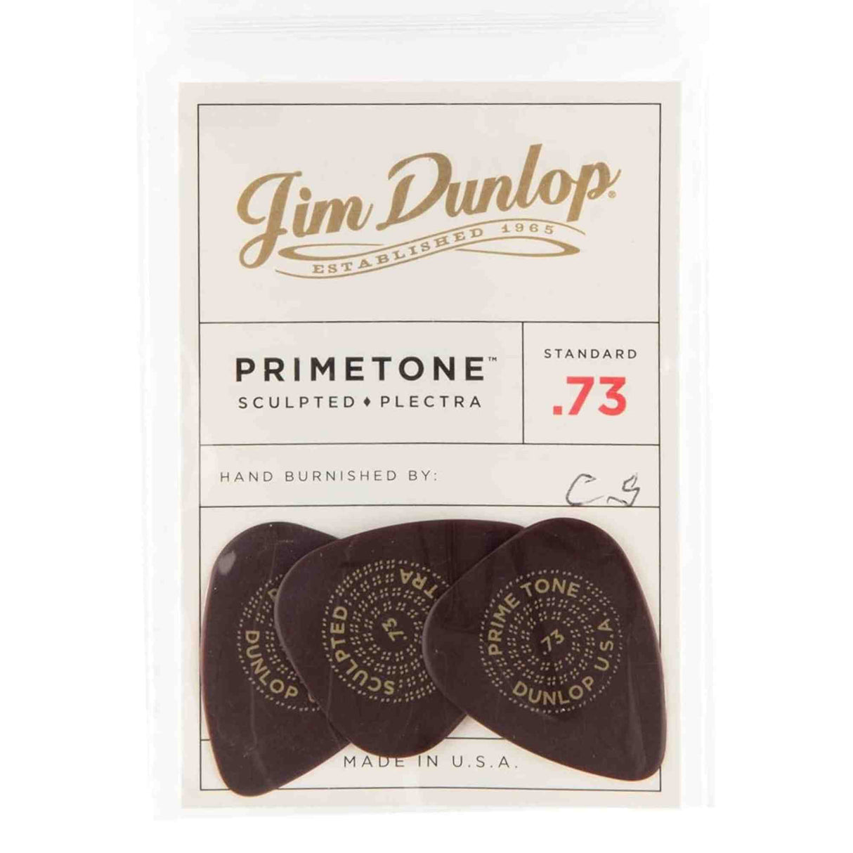 The image shows a package of three Jim Dunlop Primetone guitar picks, made in the USA. These sculpted plectra have a standard .73mm thickness (red "73" marking) and are hand burnished, featuring initials "C.G." Each dark-colored pick displays circular text including "PRIMETONE" and "DUNLOP." Known for premium tone and feel, these picks are favored by serious guitarists.