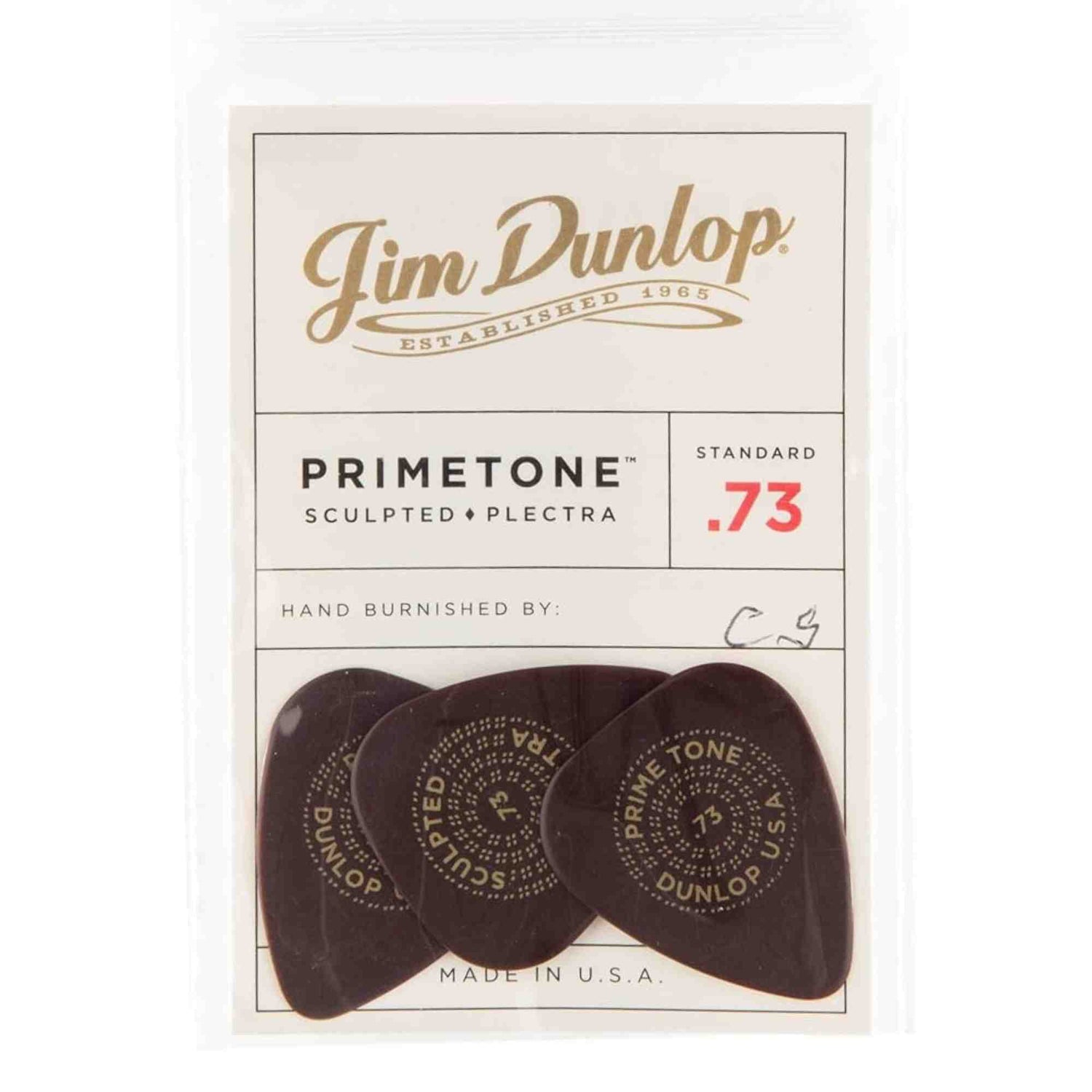 The image shows a package of three Jim Dunlop Primetone guitar picks, made in the USA. These sculpted plectra have a standard .73mm thickness (red "73" marking) and are hand burnished, featuring initials "C.G." Each dark-colored pick displays circular text including "PRIMETONE" and "DUNLOP." Known for premium tone and feel, these picks are favored by serious guitarists.