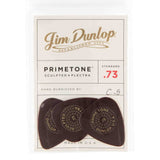 The image shows a package of three Jim Dunlop Primetone guitar picks, made in the USA. These sculpted plectra have a standard .73mm thickness (red "73" marking) and are hand burnished, featuring initials "C.G." Each dark-colored pick displays circular text including "PRIMETONE" and "DUNLOP." Known for premium tone and feel, these picks are favored by serious guitarists.