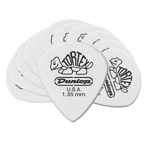 The image shows a collection of white Dunlop Tortex guitar picks featuring the turtle logo and text reading "TORTEX," "Dunlop," "U.S.A.," and "1.35 mm." These 1.35mm picks are relatively thick, offering a firm feel and bright tone. Known for durability, grip, and consistent performance, Tortex picks with their white color and tortoiseshell design are popular among guitarists.