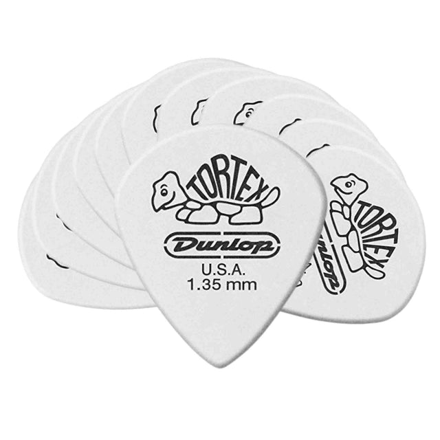 The image shows a collection of white Dunlop Tortex guitar picks featuring the turtle logo and text reading "TORTEX," "Dunlop," "U.S.A.," and "1.35 mm." These 1.35mm picks are relatively thick, offering a firm feel and bright tone. Known for durability, grip, and consistent performance, Tortex picks with their white color and tortoiseshell design are popular among guitarists.