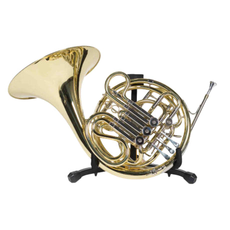 The image shows a French horn, a brass wind instrument with a circular, coiled design. Visible are the large flared bell on the left, intricate tubing loops, four black valves, and the mouthpiece receiver. The horn rests upright on a black stand, displaying its shiny golden brass finish. Known for its warm tone and wide range, it is a key orchestra instrument and notable for its playing challenges.