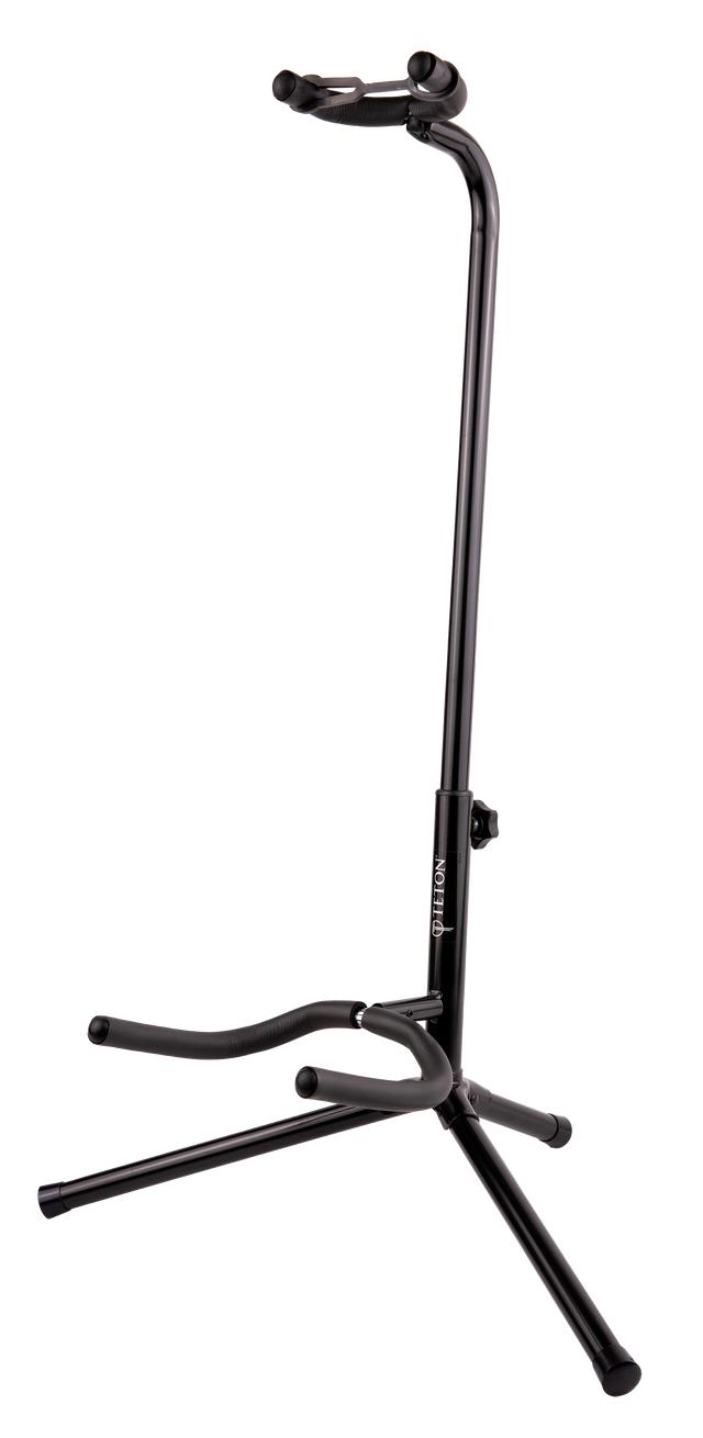 The image shows a black TETON guitar stand with a tripod base and adjustable vertical pole. It has padded curved yokes to cradle the guitar’s body and a lower support arm for the guitar’s bottom. Designed for acoustic or electric guitars, the stand offers stable, secure storage and protection from scratches, making it ideal for home, studio, or stage use.