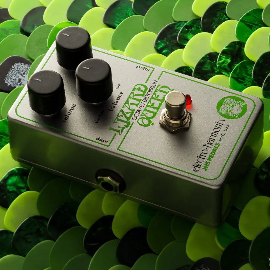 A slanted view of the Elecro-Harmonix Lizard Queen Nano pedal with green lettering and artwork. The pedal is sitting on a background of green picks.
