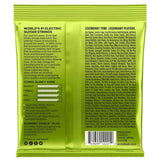 The image shows the back of a bright green Ernie Ball Slinky electric guitar strings package. It highlights the "World’s #1 Electric Guitar Strings" with 60+ years of heritage, made in Coachella, CA. Features include nickel-plated steel wrap wire, "Element Shield Plus" corrosion protection, and a frequency response chart. The package also lists famous users like Eric Clapton and Jimmy Page, along with a barcode and social media info.