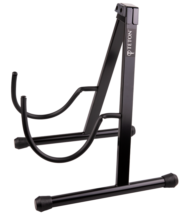 The image shows a Teton floor-standing guitar stand with a black metal A-frame design. It has rubber feet to prevent slipping, curved arms to hold acoustic or electric guitars securely, and a neck support for the headstock. The "TETON" logo is visible on the vertical support. Rubber padding protects the guitar's finish. This stand safely stores and displays most standard guitars, preventing damage when not in use.