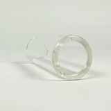 The image shows a clear glass guitar slide, a hollow cylindrical tube worn on a finger to produce smooth sliding effects on guitar strings. Common in blues and rock, glass slides create a bright, distinctive tone compared to metal slides. The slide is photographed against a neutral background, highlighting its transparent glass construction and simple shape.