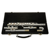 The image shows a silver-plated concert flute disassembled into head joint, body, and foot joint, neatly arranged in a black hard case with custom-fitted, dark fabric-lined compartments. The flute features polished keys with springs and pads. The case includes metal clasps and a handle. This woodwind instrument, commonly used in school bands and orchestras, appears to be a student or intermediate-level model.