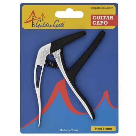 The image shows a Golden Gate guitar capo for steel-string guitars in retail blister packaging. The capo features a silver metal body with black rubber padding and a spring-loaded clamp with an ergonomic handle. The packaging has a blue background with red accents, displays the Golden Gate Bridge logo, sagamusic.com, and states it is made in China. The capo clamps the fretboard to raise pitch and change keys easily.