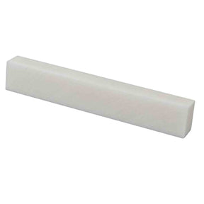 The image shows a guitar nut, a small rectangular piece at the junction of the headstock and fretboard. Made from white or cream material like bone or synthetic bone, it spaces and supports the strings, affecting intonation and playability. The nut defines one end of the vibrating string length and is essential for setup, maintenance, and tone quality in stringed instruments.