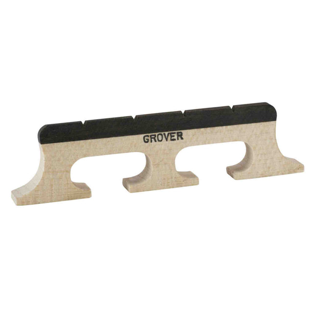 The image shows a Grover banjo bridge made of light-colored wood, likely maple, with three arched feet resting on the banjo head. It features a black ebony cap with notches for string placement. The "GROVER" brand name is stamped on the bridge, which transfers string vibrations to the banjo head, essential for tone and projection. Grover is a renowned maker of quality banjo and guitar hardware.