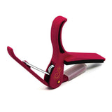 The image shows a red/burgundy guitar capo with a spring-loaded clamp and padded bar that protects the guitar neck. It features a curved shape to fit the fretboard and a visible brand logo. Designed for easy one-handed use, this quality capo raises string pitch by clamping across frets, allowing guitarists to transpose songs while using familiar chords, commonly used in acoustic and electric guitars.