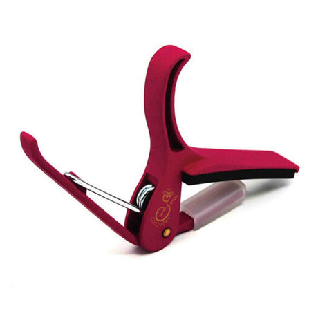 The image shows a red/burgundy guitar capo with a spring-loaded clamp and padded bar that protects the guitar neck. It features a curved shape to fit the fretboard and a visible brand logo. Designed for easy one-handed use, this quality capo raises string pitch by clamping across frets, allowing guitarists to transpose songs while using familiar chords, commonly used in acoustic and electric guitars.