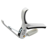 The image shows a Grover spring-loaded trigger-style guitar capo with a silver/chrome finish. It features a curved clamp, padded contact points to protect the guitar neck and strings, and a spring trigger for easy one-handed use. This professional-grade capo raises the pitch of all strings simultaneously, allowing guitarists to change keys without new fingerings, suitable for both acoustic and electric guitars.