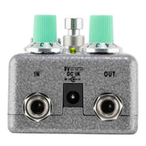 Guitar effects pedal with green knobs and metal connectors on a white background