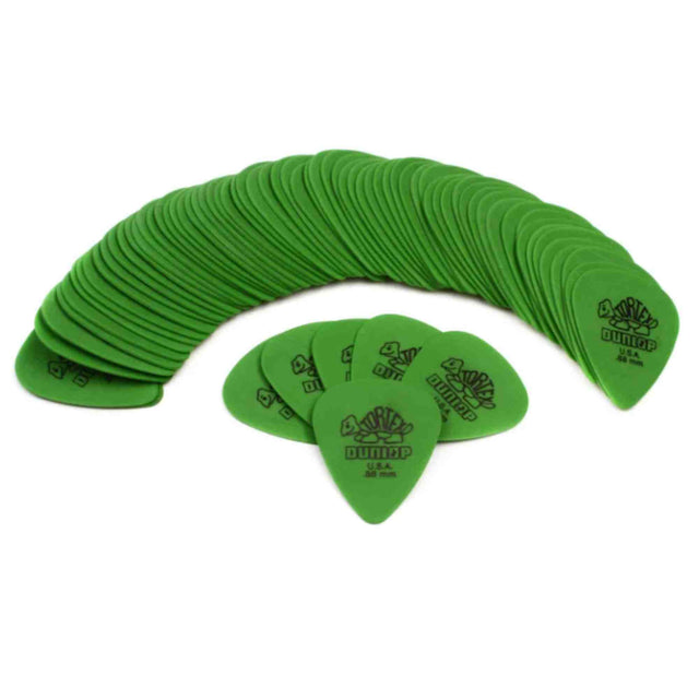 The image shows a collection of bright green Dunlop guitar picks, arranged in a large curved stack with several individual picks displayed in front, highlighting their teardrop shape. The picks feature the Dunlop logo, indicating a specific model or thickness. These essential guitar accessories are used to strum or pluck strings and come in various colors and styles to suit different playing preferences.