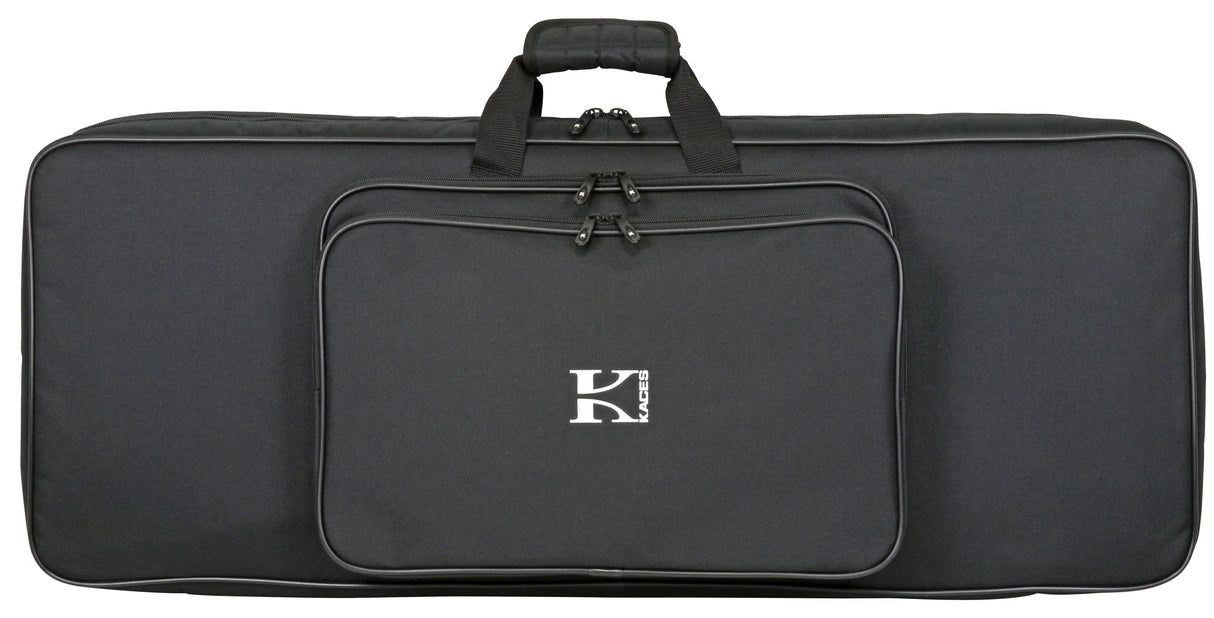 The image shows a black Kaces keyboard gig bag with the logo in white on the front. It has a padded, comfort-grip handle, multiple zippered compartments including a main keyboard section and front pocket, and black hardware. The large, rectangular soft case is designed for transporting full-size keyboards (61-88 keys) and offers a sleek, professional look for musicians on the go.