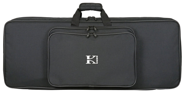 The image shows a black Kaces keyboard gig bag with the logo in white on the front. It has a padded, comfort-grip handle, multiple zippered compartments including a main keyboard section and front pocket, and black hardware. The large, rectangular soft case is designed for transporting full-size keyboards (61-88 keys) and offers a sleek, professional look for musicians on the go.