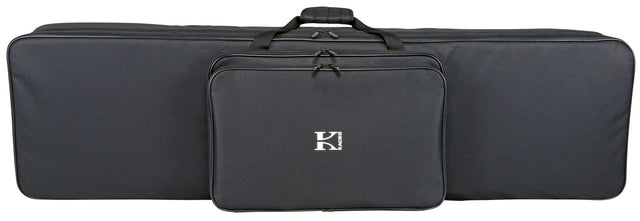 The image shows a Korg soft-shell keyboard gig bag in black fabric with a "K" logo on the front zippered pocket. It features a large main compartment for a keyboard, top carry handles, and a long rectangular shape. Designed for easy transport, it protects electronic keyboards from dust, moisture, and minor impacts while storing accessories like cables and pedals in the front pocket.