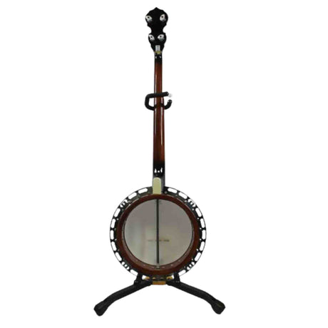 The image shows a 5-string banjo with a circular body and white drumhead, a long reddish-brown wooden neck, and a black headstock with tuning pegs. It has metal hardware including a tailpiece and tension brackets around the rim. The instrument rests on a black tripod stand and features a strap attachment on the neck. Common in bluegrass and folk music, it combines string and percussion elements with roots in American and African musical traditions.