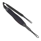 The image shows a black guitar strap with a wide padded shoulder section for comfort, adjustable length via metal buckles, and brown leather end tabs for secure attachment. Made from durable fabric webbing, it features metal hardware for connecting to the guitar. This practical strap helps distribute the guitar’s weight, reducing fatigue during extended playing, and is suitable for acoustic, electric, or bass guitars.