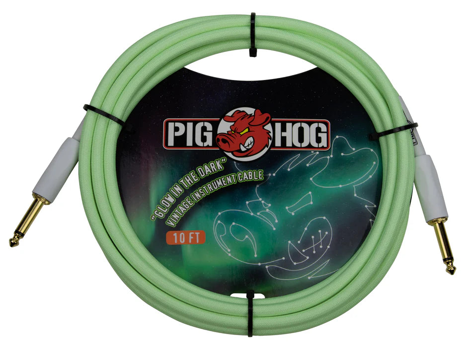 The image shows a coiled Pig Hog "Glow in the Dark" vintage 10-foot instrument cable with light green color and gold-plated 1/4" connectors with white housings, secured by black ties. The packaging features the Pig Hog logo with a red boar head and artwork of a glowing guitar on a dark background. This cable is used to connect electric guitars and other instruments to amplifiers or pedals.