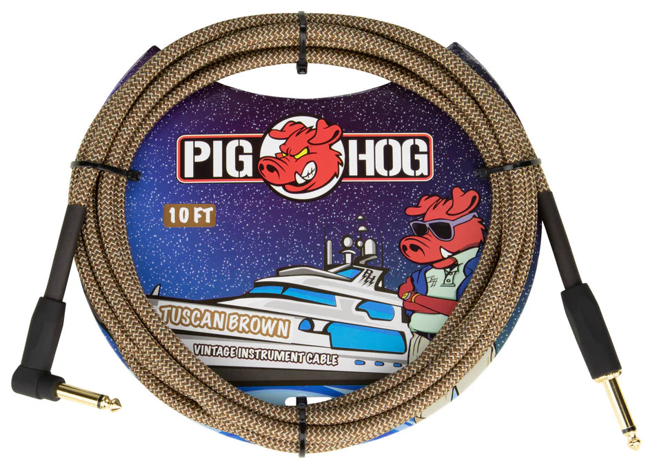 The image shows a Pig Hog "Tuscan Brown" vintage-style instrument cable. It is a 10-foot braided brown/tan cable with gold-plated 1/4" jack connectors on both ends, designed for guitars, basses, or pedals. The packaging features Pig Hog’s cartoon pig mascot and space-themed art, highlighting its retro look and reliable signal transmission favored by musicians.