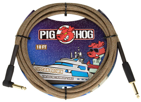 The image shows a Pig Hog "Tuscan Brown" vintage-style instrument cable. It is a 10-foot braided brown/tan cable with gold-plated 1/4" jack connectors on both ends, designed for guitars, basses, or pedals. The packaging features Pig Hog’s cartoon pig mascot and space-themed art, highlighting its retro look and reliable signal transmission favored by musicians.
