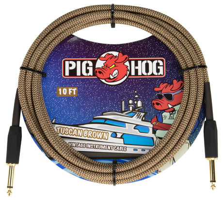 The image shows a Pig Hog Tuscan Brown 10-foot instrument cable with gold-plated 1/4" connectors on both ends. It features a woven brown/tan braided fabric jacket, vintage-style design, and Pig Hog’s red pig mascot logo. The professional packaging has colorful yacht-themed graphics. This durable, high-quality cable is designed for guitars, basses, and other instruments, offering reliable signal transfer and protection for studio or live use.