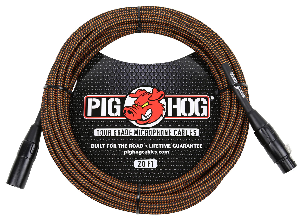 The image shows a Pig Hog tour-grade 20-foot microphone cable with black and orange braided sleeve. It features XLR male to female connectors and a label displaying the Pig Hog red pig logo, "Built for the Road," and "Lifetime Guarantee." Designed for durability, this professional cable is ideal for live sound and touring musicians.