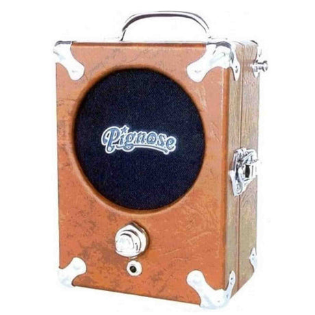The image shows a Pignose portable guitar amplifier with a compact, vintage-style wooden body, metal corner protectors, a dark speaker grille featuring the white "Pignose" logo, a single control knob, a small input jack, and a carrying handle. Known for its portable, battery-powered design since the 1970s, it delivers surprisingly full, tube-like sound despite its small size.