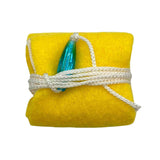 The image shows a musical instrument cleaning kit featuring a folded yellow microfiber cloth tied with white cord and a blue-green cleaning swab tucked inside. The lint-free cloth is ideal for safely cleaning wind and string instruments, removing moisture and dust while protecting finishes. The compact bundle is portable, making it a practical accessory for maintaining instruments in good condition.