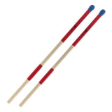 The image shows a pair of drum rods, also called bundled sticks or multi-rods, made of thin wooden dowels bound with red grip tape and featuring blue rubber tips. These percussion accessories offer a softer, controlled sound with good articulation, popular in acoustic and jazz settings. The red wrap secures the rods and provides grip, while the blue tips protect both the rods and drum heads during play.