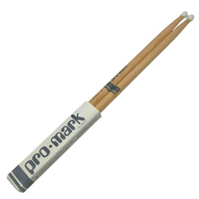 The image shows a pair of Pro-Mark wooden drumsticks with white nylon tips in their original packaging. They have a natural wood finish with Pro-Mark branding and a model number on the shaft. The white tips are favored for producing a brighter cymbal sound and greater durability compared to wooden tips.