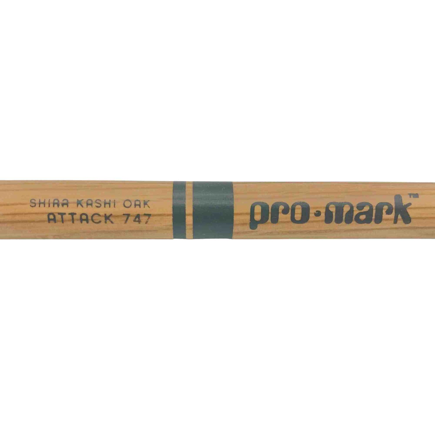 The image shows a Pro-Mark "Attack 747" drumstick made from Shira Kashi Oak wood. It has a natural wood finish with dark grip banding. Shira Kashi Oak is a dense, durable Japanese oak favored for drumsticks, offering greater hardness than American hickory. Pro-Mark is a well-known drumstick brand, and the "Attack 747" model specifies its size, tip shape, and playing style, making it a percussion accessory.