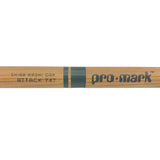 The image shows a Pro-Mark "Attack 747" drumstick made from Shira Kashi Oak wood. It has a natural wood finish with dark grip banding. Shira Kashi Oak is a dense, durable Japanese oak favored for drumsticks, offering greater hardness than American hickory. Pro-Mark is a well-known drumstick brand, and the "Attack 747" model specifies its size, tip shape, and playing style, making it a percussion accessory.