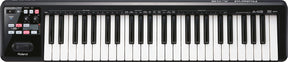 The image shows a Roland A-49 MIDI keyboard controller with 49 standard piano keys and a black casing. It features a control panel on the left with a power button, transport controls (play, stop, record), various parameter buttons, and a small display. Designed for music production, it controls software instruments and DAWs, making it popular for studio and live use due to its compact, portable design.