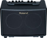 The image shows a compact Roland acoustic guitar amplifier with a black textured front grille and the Roland logo. It has six control knobs on the top panel, a sturdy black carrying handle, and "ACOUSTIC GUITAR AMP" text visible. Designed for acoustic guitar players, this portable practice amp offers clean sound and built-in effects for small venues, practice, or recording.