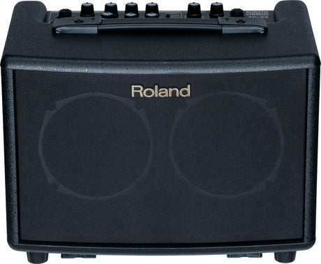 The image shows a compact Roland acoustic guitar amplifier with a black textured front grille and the Roland logo. It has six control knobs on the top panel, a sturdy black carrying handle, and "ACOUSTIC GUITAR AMP" text visible. Designed for acoustic guitar players, this portable practice amp offers clean sound and built-in effects for small venues, practice, or recording.
