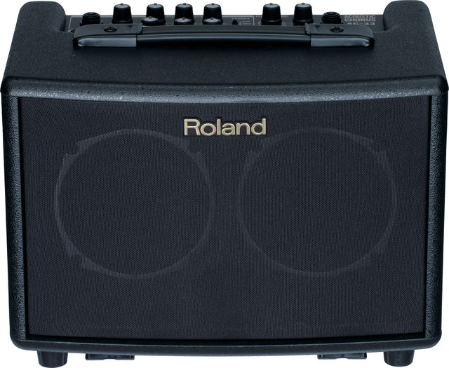 The image shows a compact Roland acoustic guitar amplifier with a black textured front grille and the Roland logo. It has six control knobs on the top panel, a sturdy black carrying handle, and "ACOUSTIC GUITAR AMP" text visible. Designed for acoustic guitar players, this portable practice amp offers clean sound and built-in effects for small venues, practice, or recording.