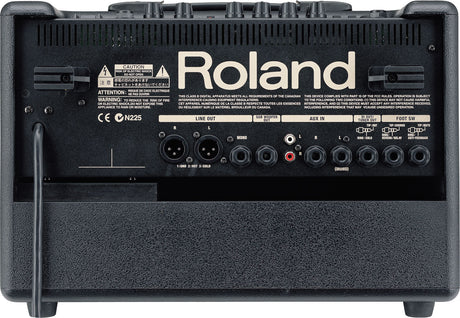 The image shows the back panel of a Roland guitar amplifier featuring a prominent logo, multiple input/output connections including LINE OUT (XLR), SUB WOOFER, AUX IN, 1/4" jacks, and footswitch ports. It has control knobs along the top, safety and certification labels, ventilation grilles, and a black textured finish. This modern amp offers extensive connectivity for live or studio use.