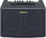 The image shows a compact black Roland guitar amplifier with gold branding on the front grille. It has six black control knobs and additional switches on the top panel, along with a carrying handle. Designed for acoustic guitars, the amp features a clean, professional look with black tolex covering. Ideal for practice and small performances, it combines portability with quality sound, suitable for beginners and professionals.