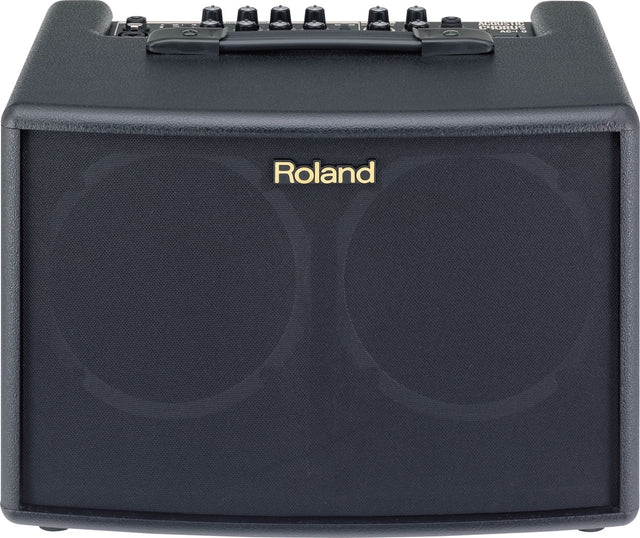 The image shows a compact black Roland guitar amplifier with gold branding on the front grille. It has six black control knobs and additional switches on the top panel, along with a carrying handle. Designed for acoustic guitars, the amp features a clean, professional look with black tolex covering. Ideal for practice and small performances, it combines portability with quality sound, suitable for beginners and professionals.