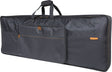 The image shows a Roland keyboard gig bag, a large, professional soft case for protecting and transporting keyboards. It has a sleek black design with orange accents, the Roland logo, padded comfort handles, multiple exterior pockets for accessories, and is made from durable nylon material. The long, rectangular shape is typical for keyboard cases, ideal for musicians on the move.